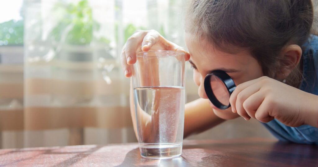 Enfant qui examine un verre d'eau avec une loupe