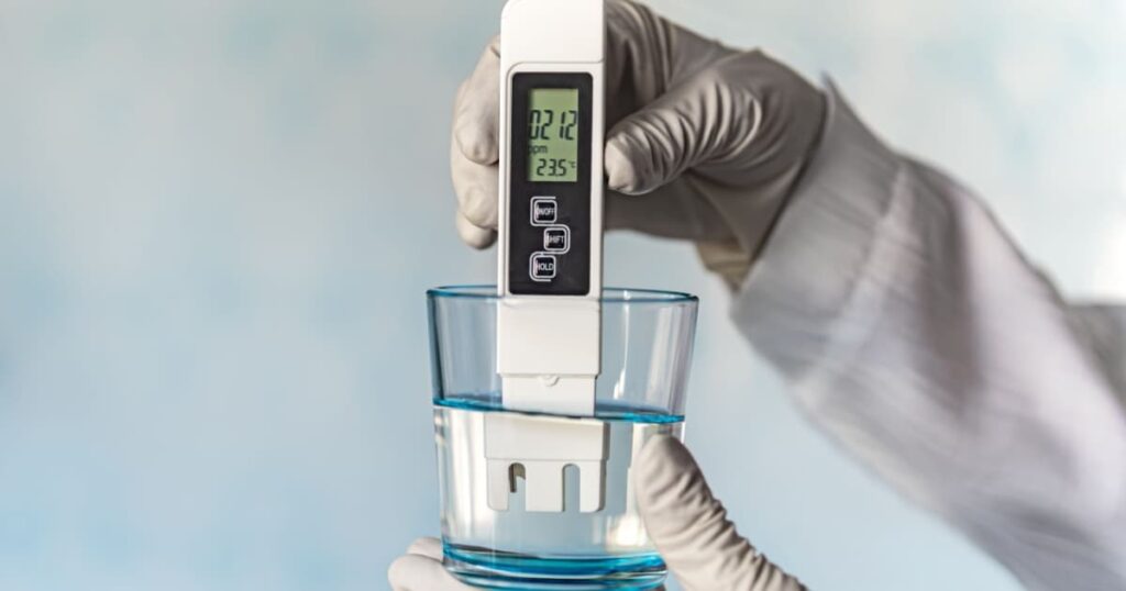 Personne qui mesure la dureté de l'eau à l'aide d'un appareil dans un verre d'eau avec des gants 