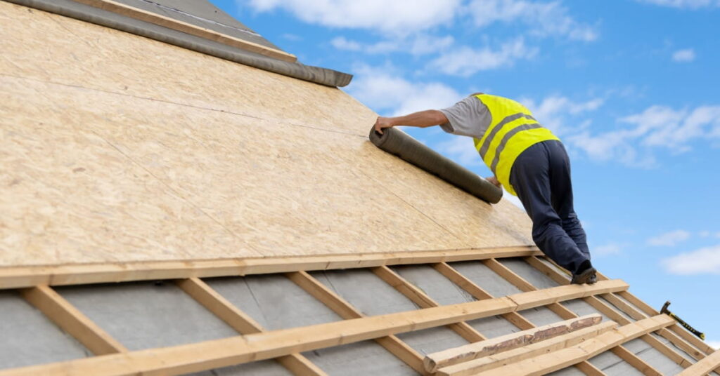 pose d'un rouleau de sous toiture sur un toit par un homme