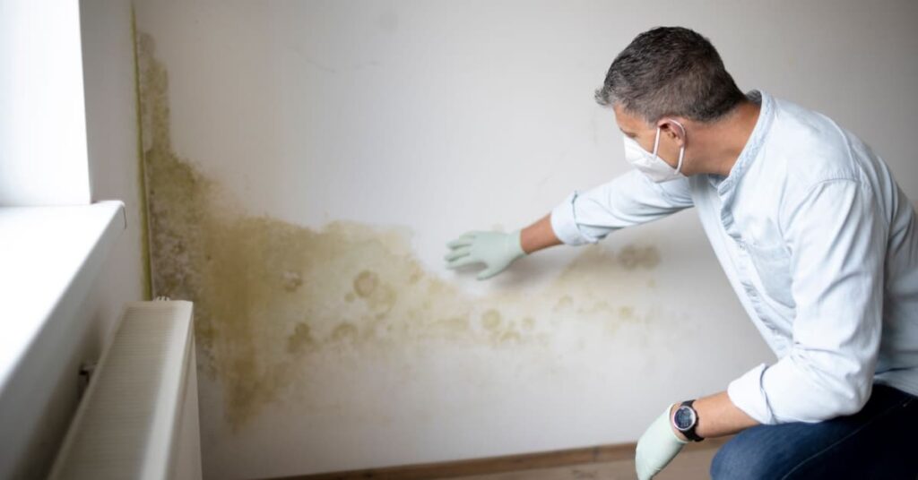 Homme avec masque constatant la présence d'humidité dans un mur.